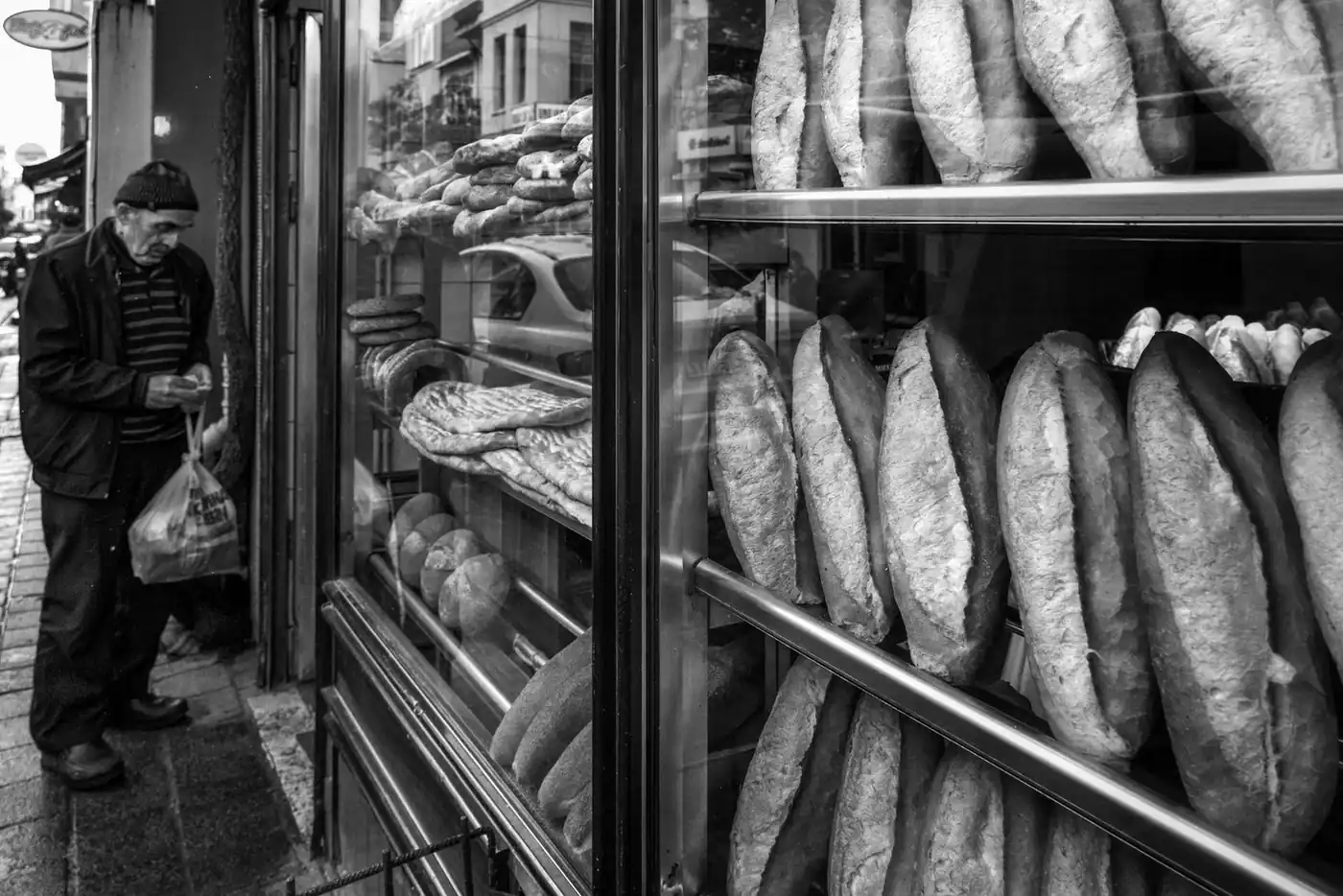 A black and white image of a bakery storefront featuring various breads with a person shopping outside.