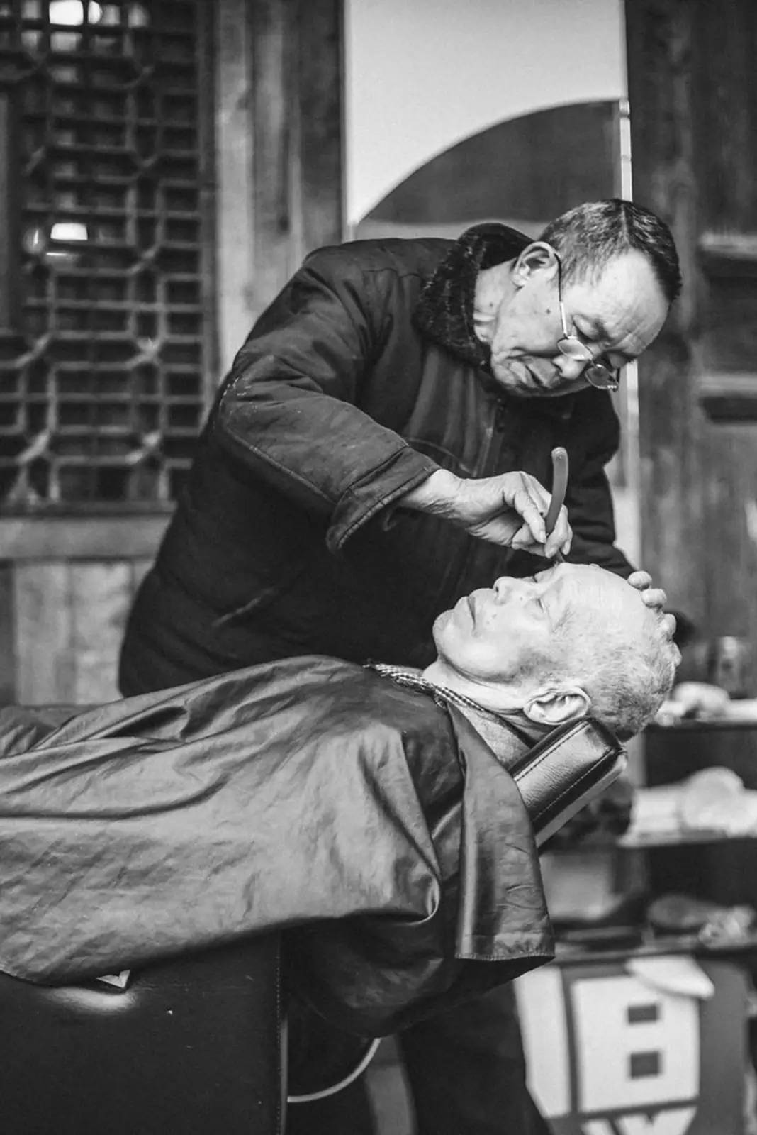 An elderly man receives a shave in a vintage barbershop setting.