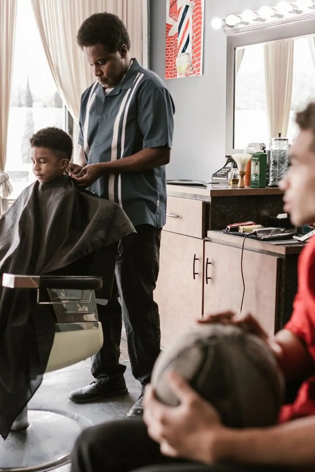 Barber expertly styling young boy's hair in a lively barbershop atmosphere.