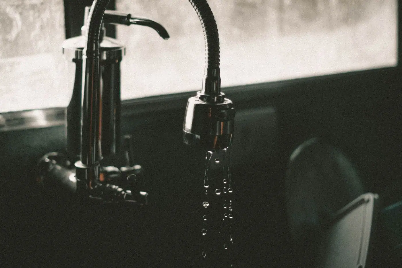 Close-up of a kitchen faucet with water droplets falling into the sink, captured in a minimalist style.