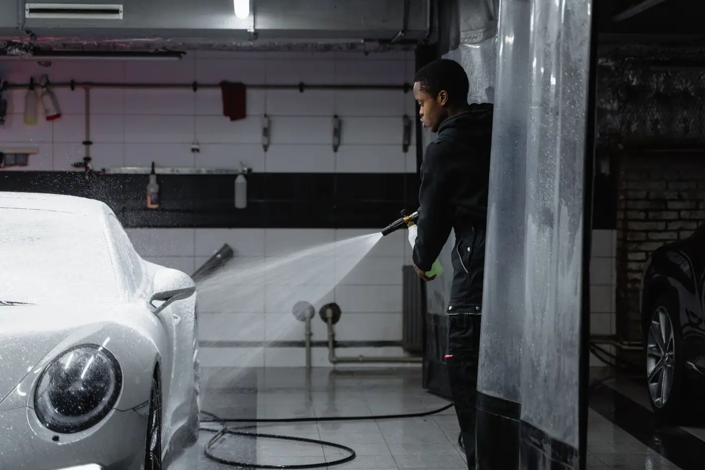 A person using a pressure washer to clean a car in an indoor garage.