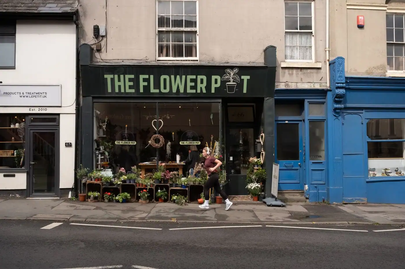 A flower shop front on a sunny high street with a passer-by