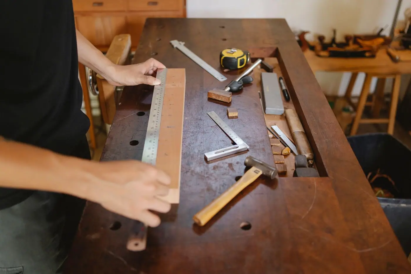Carpenter measuring a timber plank with a ruler, with a hammer and tools on the table
