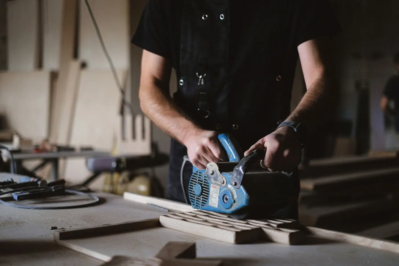 Carpenter using a belt sander on a wooden plank at a joinery workbench