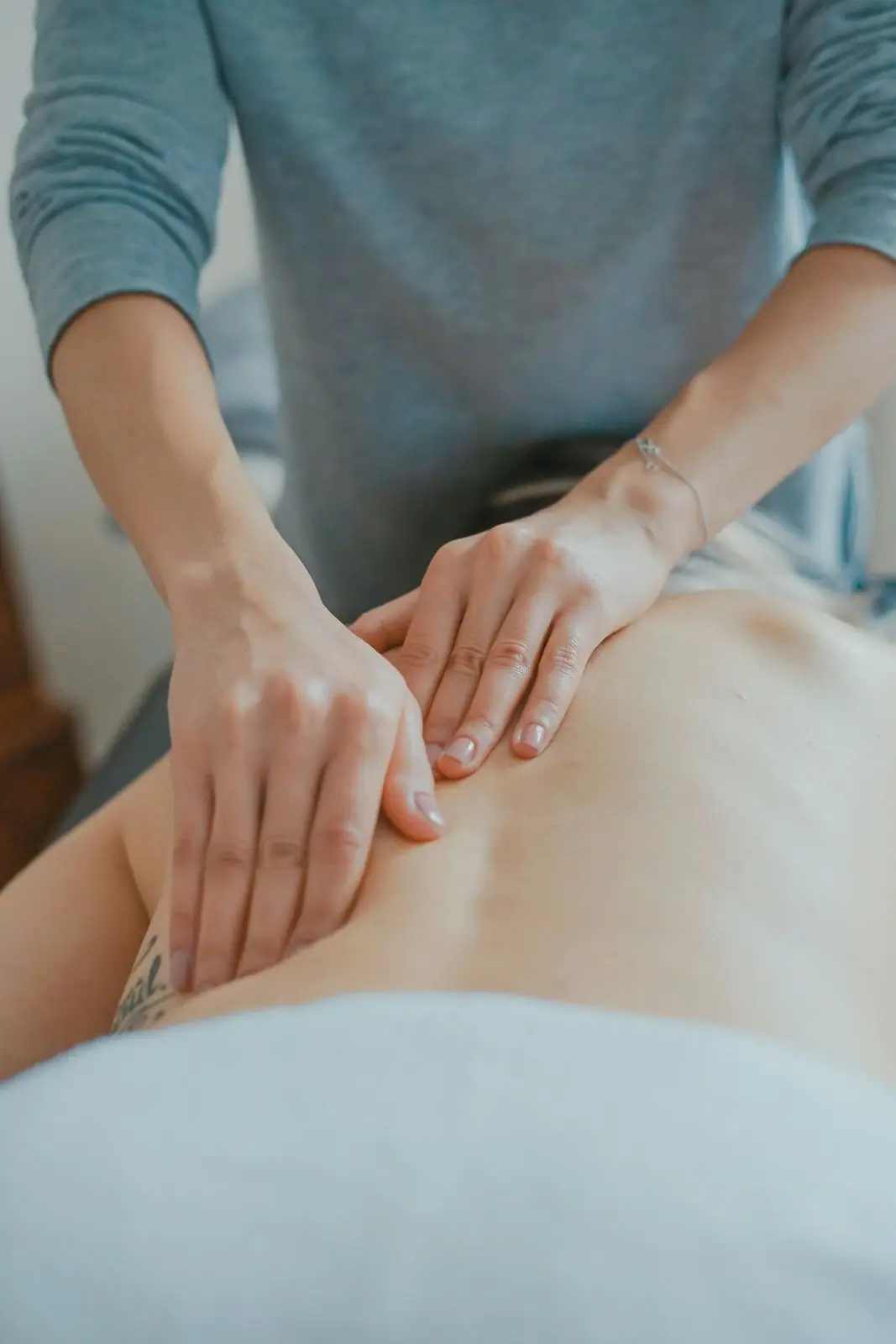 Close-up of a therapist's hands using both thumbs to apply pressure to a client's lower back during a massage