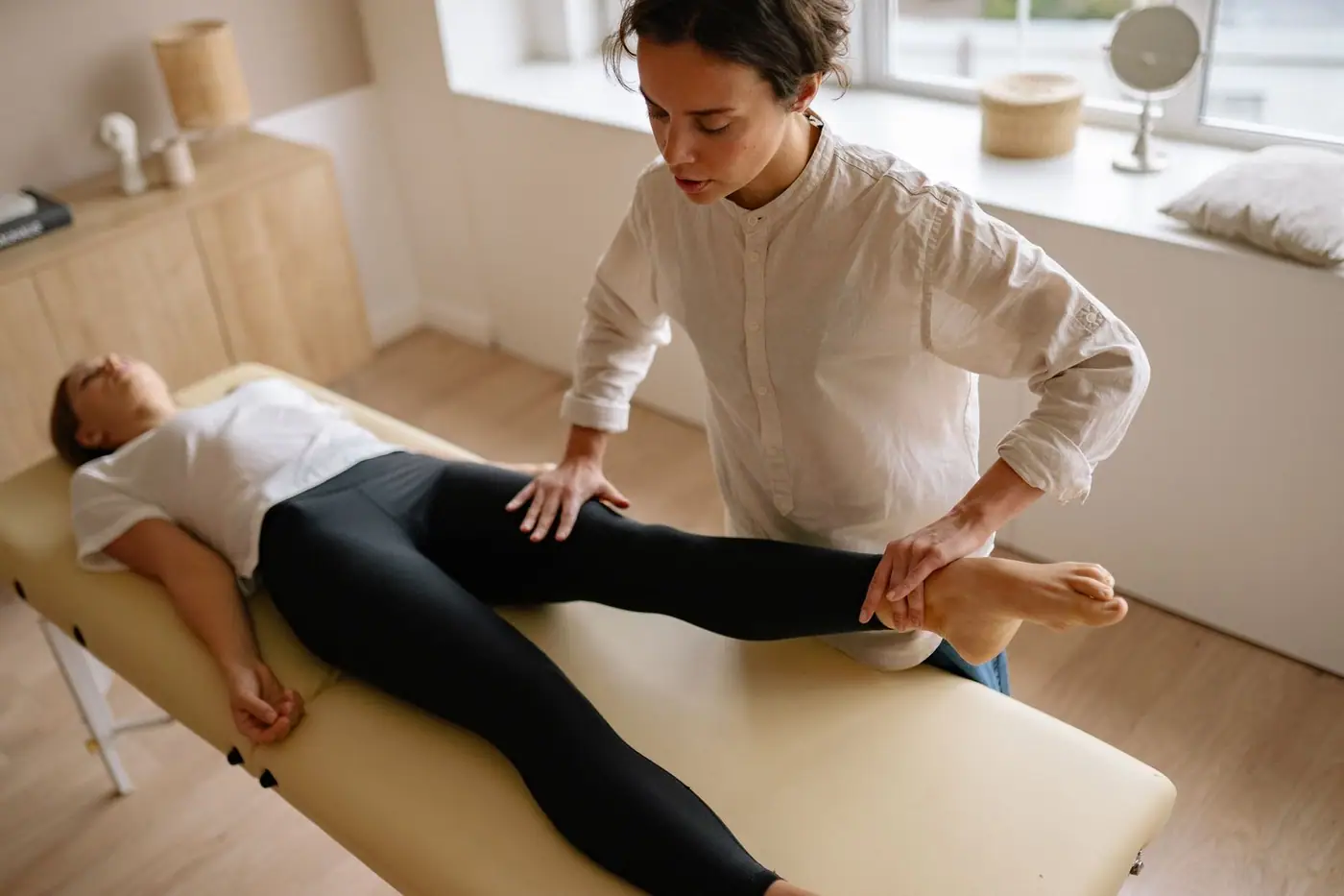 A calm treatment room where a therapist assists a woman with leg therapy