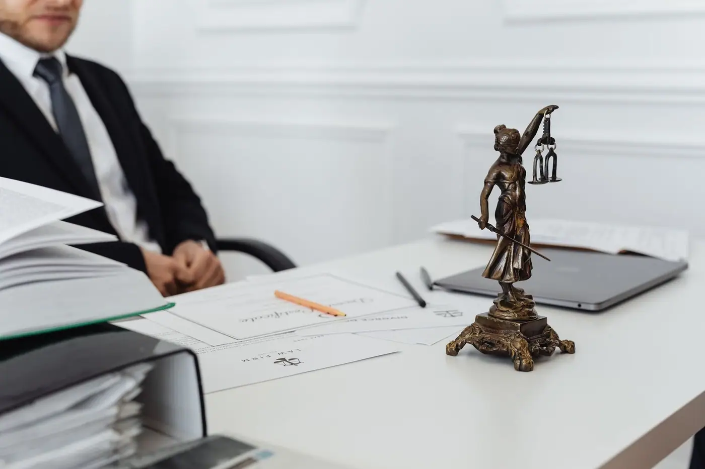 A legal professional's workspace with a Lady Justice statue, documents and a laptop.
