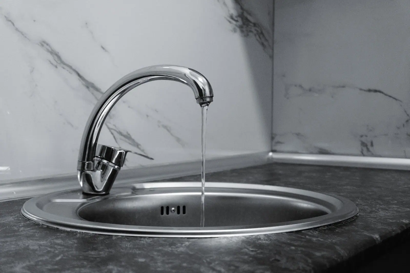 Chrome faucet with running water in a modern kitchen with marble countertop.