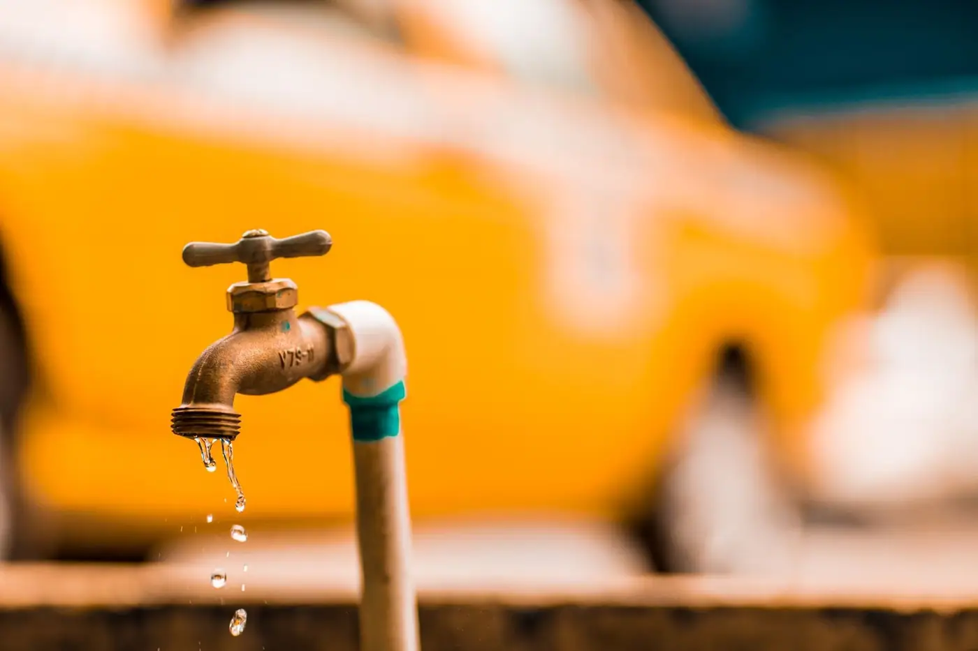 Close-up of a brass tap with water droplets against a warm yellow background