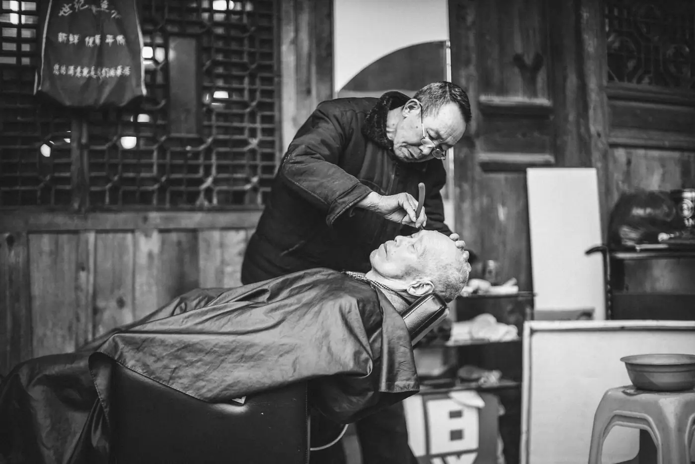 An elderly man receives a shave in a vintage barbershop setting