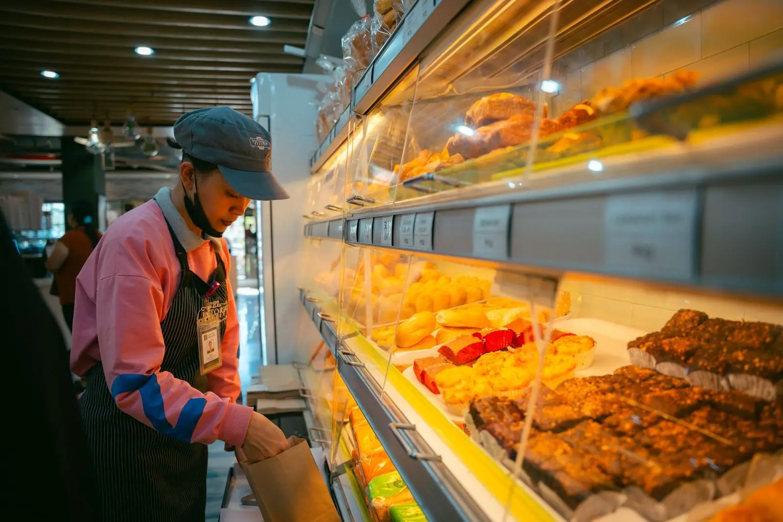 A bakery employee wears an apron and organizes pastries in a well-lit Baguio store