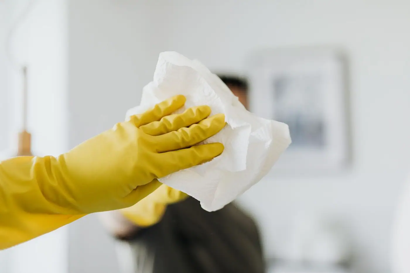 Gloved hand wiping a bathroom mirror with a paper napkin