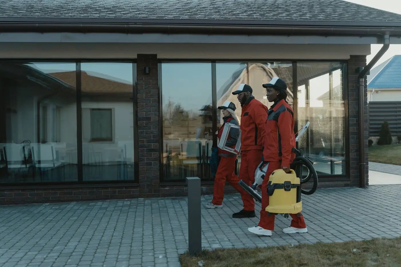A cleaning team in uniforms with equipment approaching a glass-fronted house